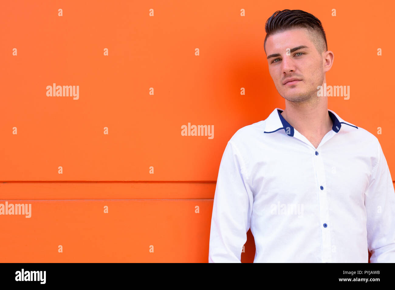 Ritratto di giovane uomo bello contro orange parete in calcestruzzo Foto Stock