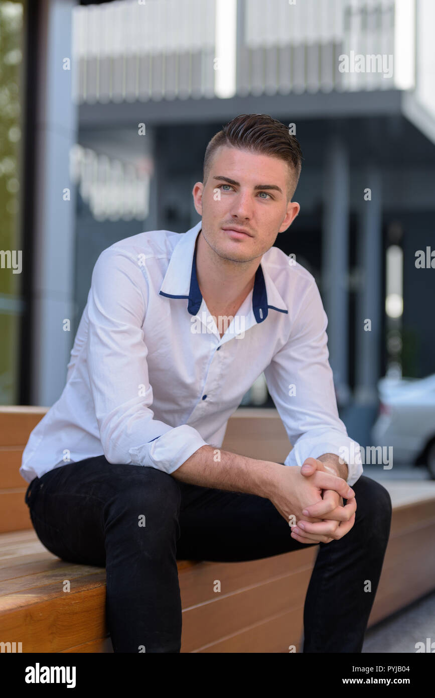 Giovane uomo bello seduto e il pensiero sulla sedia in legno all'esterno Foto Stock