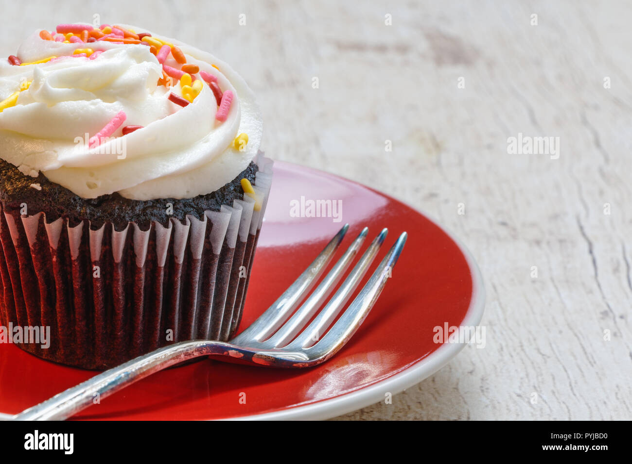 Cupcake al cioccolato con glassa alla vaniglia e spruzza su una targhetta rossa con la forcella su un leggero Sfondo legno close up Foto Stock