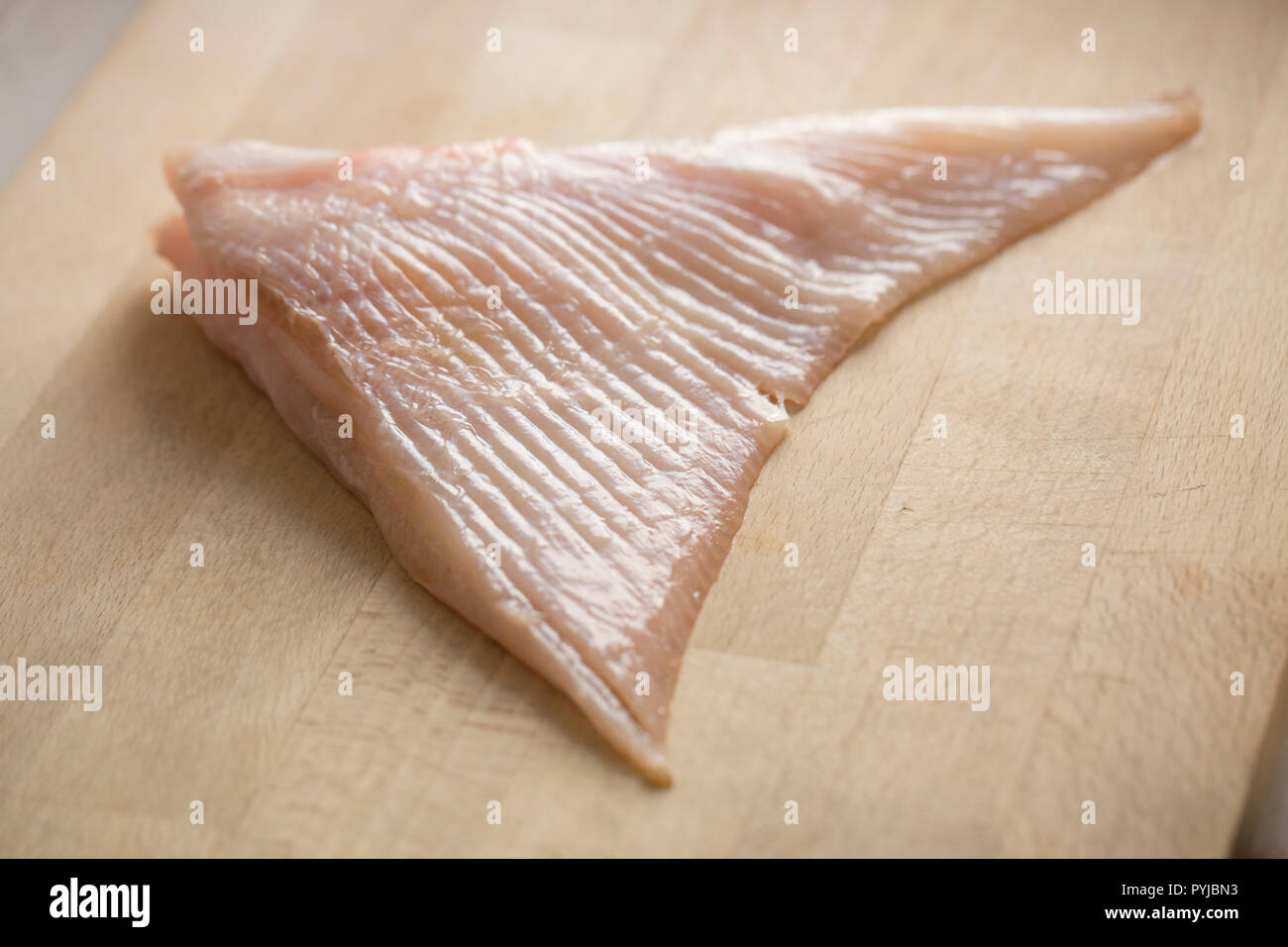 Una sezione di un raw ray ala da una razza ondulata Raja undulata, che è stata scuoiata ed è pronto per la cottura viene visualizzata su un tagliere di legno. Foto Stock