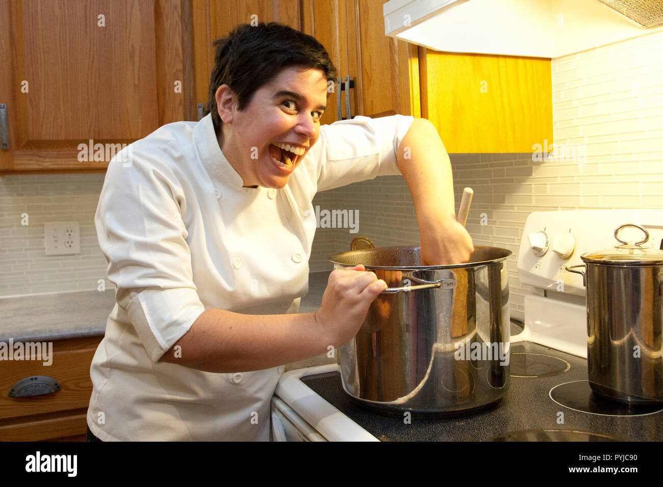Chef presso la stufa ha una vasta eyed insane sorriso come ella suscita la pentola Foto Stock