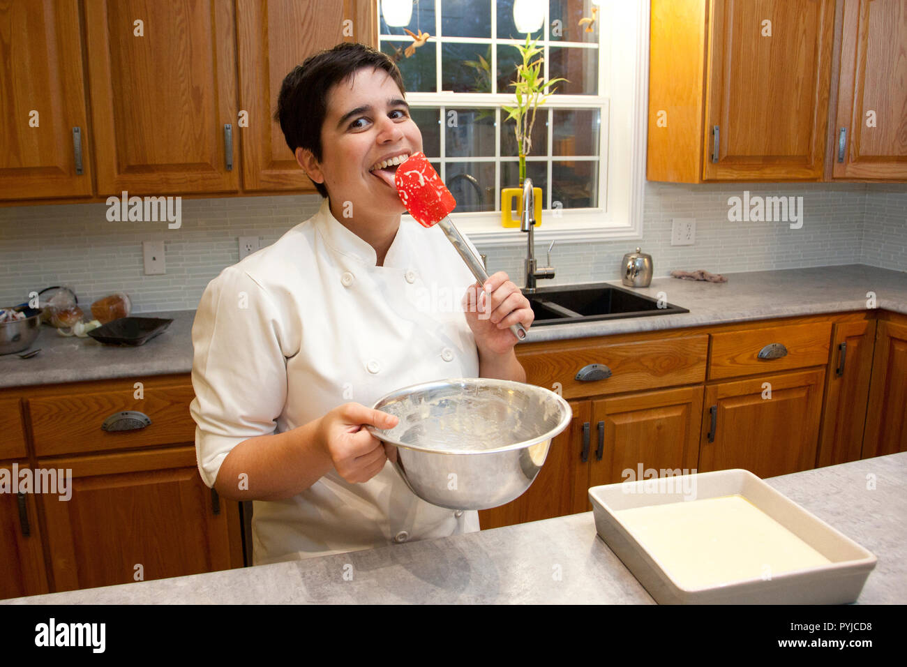 Persona in un chef's outfit sorrisi come essi leccare la spatola in cucina dopo la cottura Foto Stock