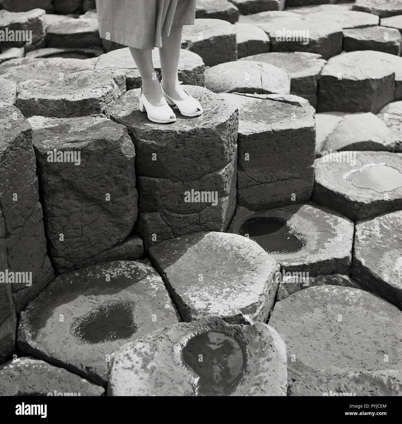 Degli anni Cinquanta, storico di close-up di una signora di piedi piedi su uno degli antichi il blocco esagonale di basalto della colonna al famoso Giant's Causeway in Co. Antrim, Irlanda del Nord, Regno Unito. La causeway sul Co. Costa di Antrim è una spettacolare meraviglia naturale e ha una stima di 40.000 di tali colonne risultanti da un'origine vulcanica eruzione fissurale. Foto Stock