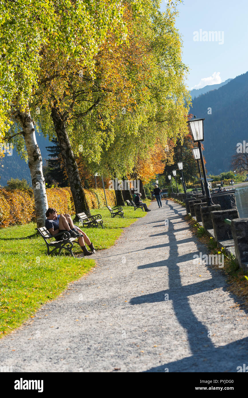 Persone appoggiano sulle panchine al sole tra autunno alberi colorati sul lago sul lago di Schliersee, Baviera, Germania Foto Stock