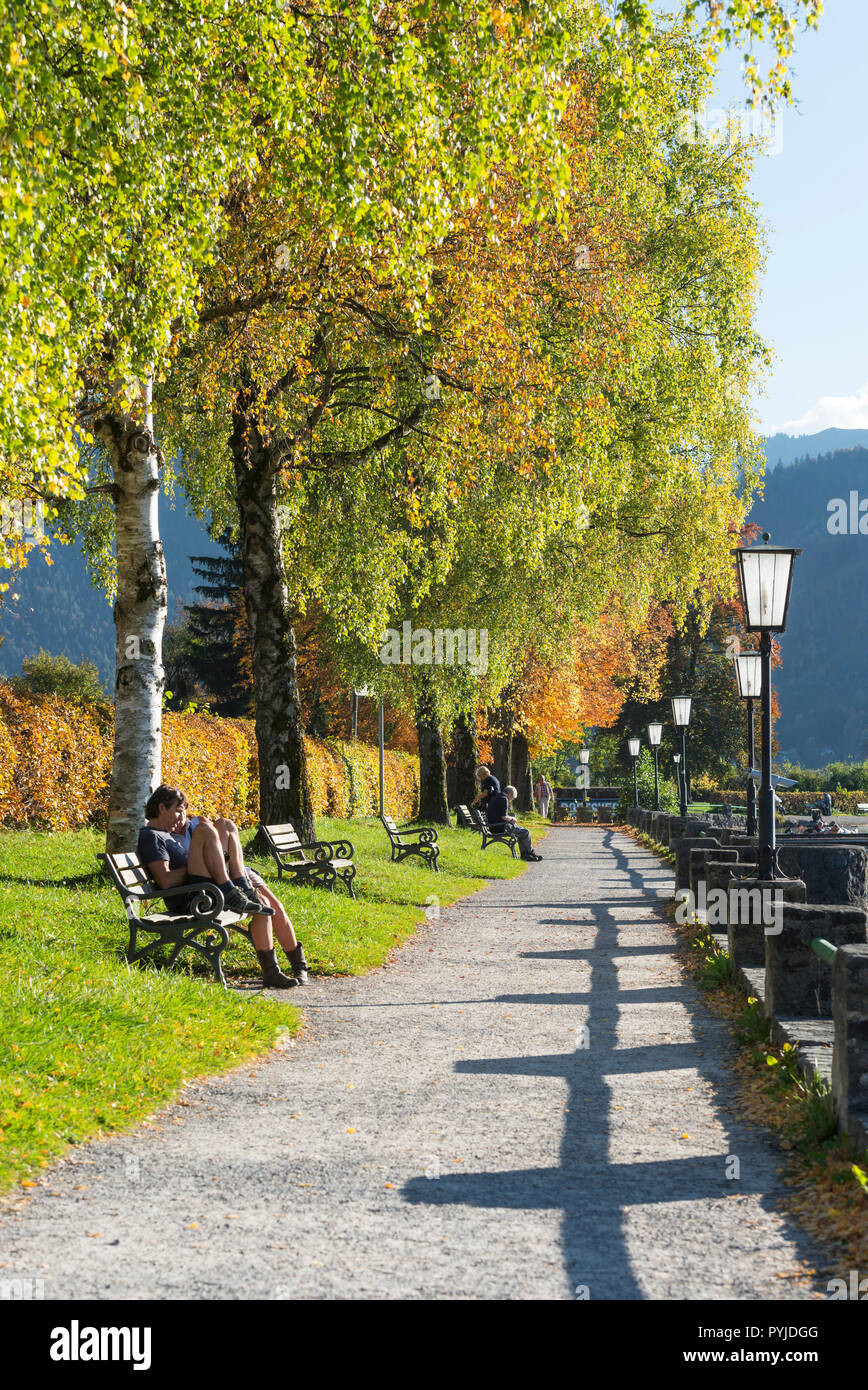 Persone appoggiano sulle panchine al sole tra autunno alberi colorati sul lago sul lago di Schliersee, Baviera, Germania Foto Stock