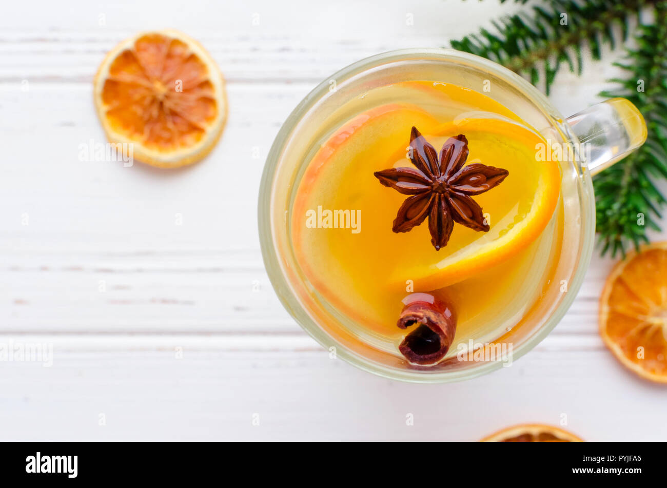 Bianco caldo vin brulé in vetro con Orange, bastoncini di cannella e anice stellato con ingredienti in bianco sullo sfondo di legno. Piccante bevanda calda. Stagionale Foto Stock