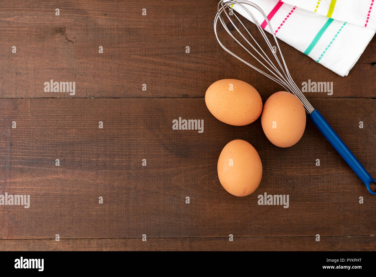 Tre uova a un filo di acciaio, frusta su un sfondo di legno, con copia spazio. Foto Stock