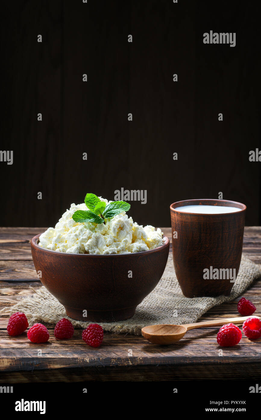 Cottage di formaggio e di latte in clayware sul tavolo di legno, cilicio table-igienico e cucchiaio di legno Foto Stock