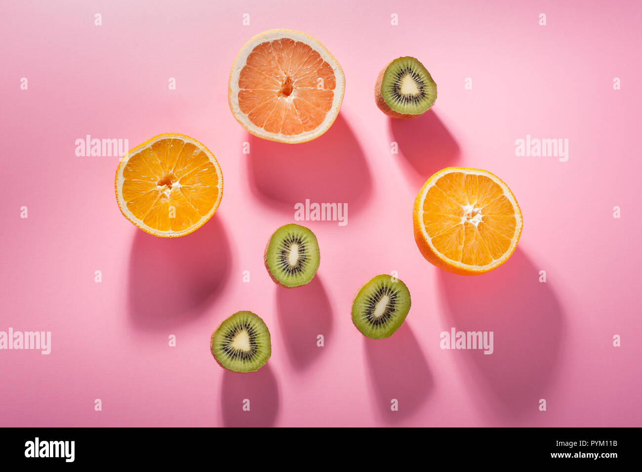 I frutti con livelli elevati di Vitamina C-- kiwi, di arancia e di pompelmo--in illuminazione diretta su un sfondo rosa. Foto Stock