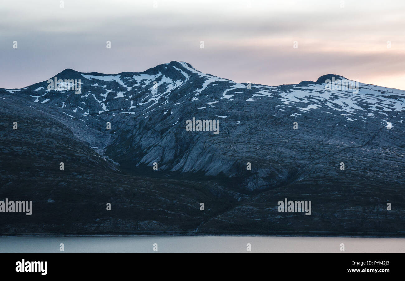 Il sole di mezzanotte incandescente dietro la montagna a un fiordo norvegese Foto Stock