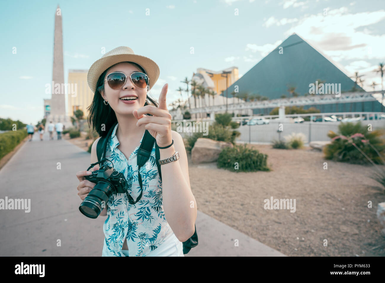Fotografo turistica puntando verso il cielo blu in piedi davanti alle piramidi a Las Vegas. Donna asiatica sorridente nel cappello e occhiali da sole. vacanze estive Foto Stock