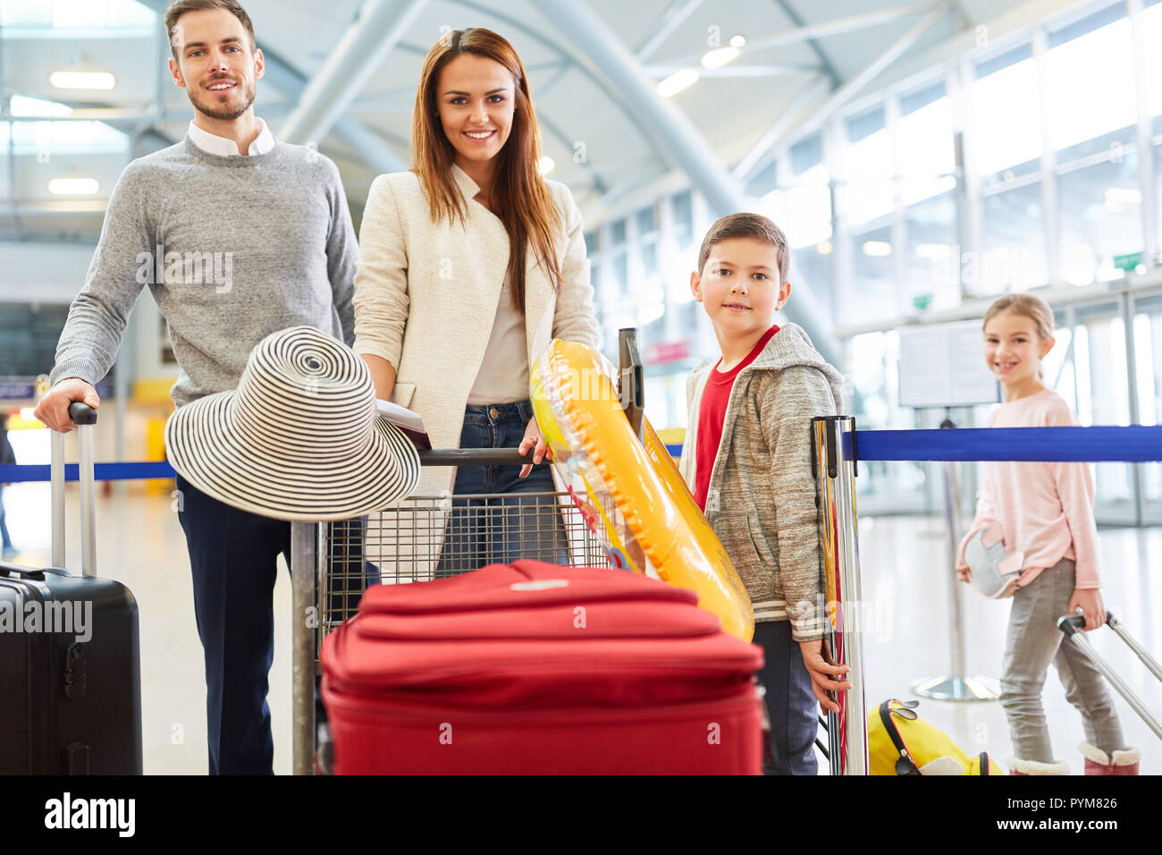 La famiglia felice con i bambini e con i bagagli è impaziente di vacanza nel terminal dell'aeroporto Foto Stock