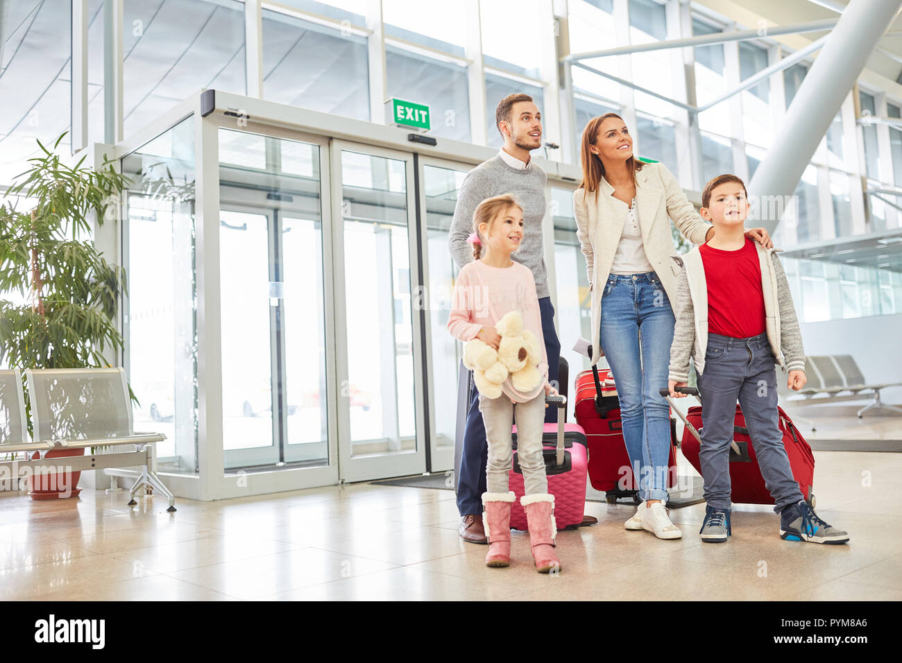 I genitori e i due bambini con i bagagli nel terminal dell'aeroporto sono alla ricerca in avanti per una vacanza in famiglia Foto Stock