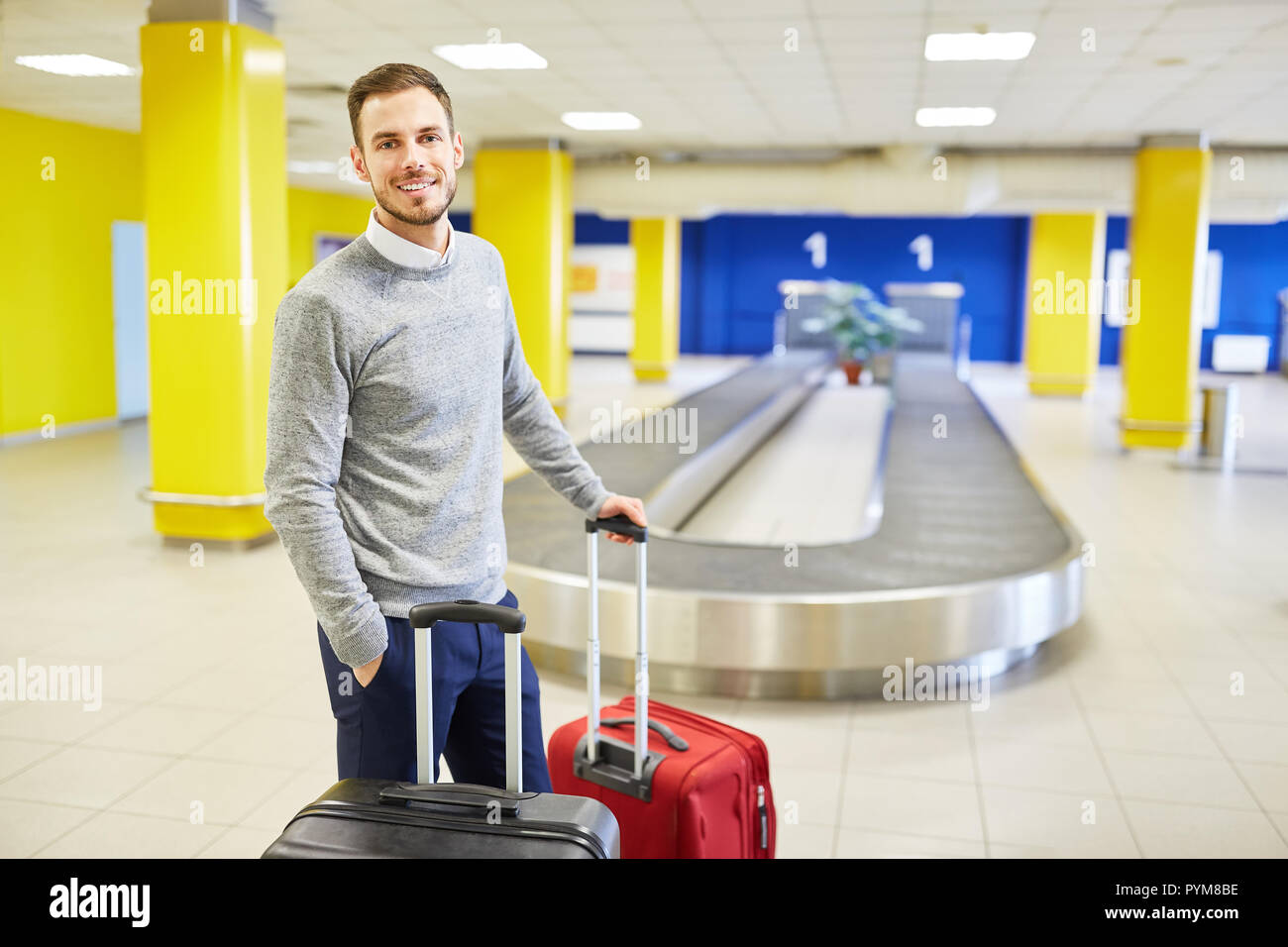 L uomo come un viaggiatore in arrivo con le valigie sul nastro bagagli nel terminal dell'aeroporto Foto Stock