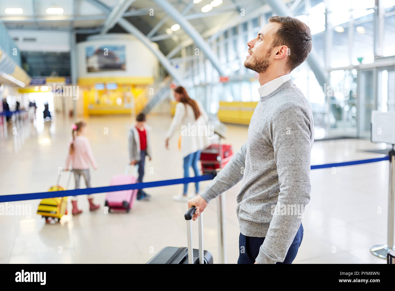 L uomo è alla ricerca per il volo di coincidenza in il terminal aeroportuale con la famiglia in background Foto Stock