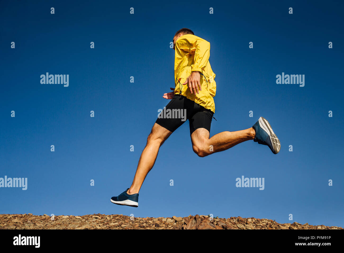 L'uomo runner in giallo giacca sportiva eseguire sul cielo blu sullo sfondo Foto Stock