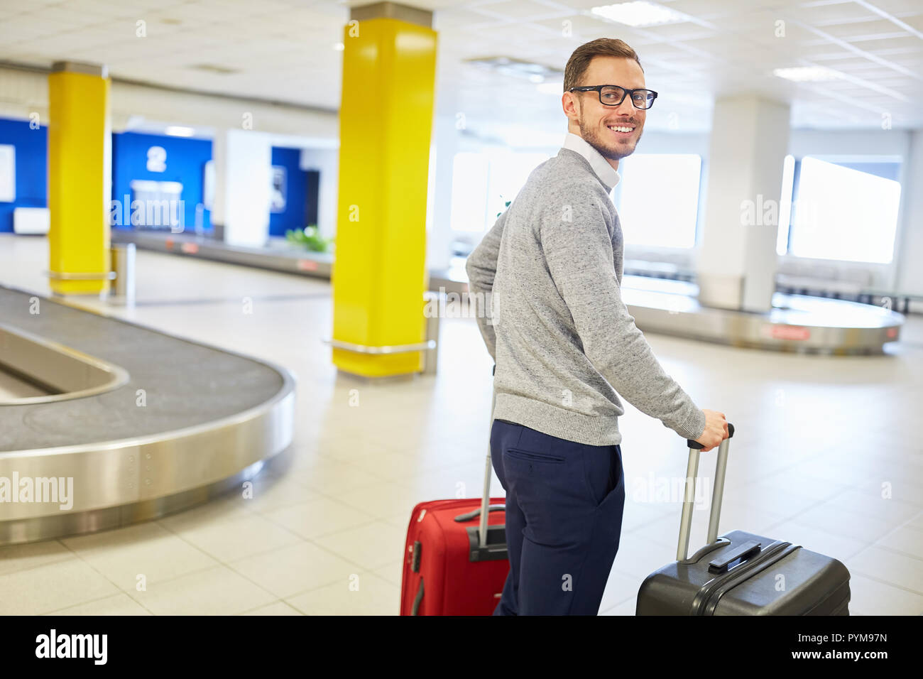 Uomo con le valigie presso l'aeroporto di reclamo per il bagaglio è di guardare avanti per il suo viaggio in vacanza Foto Stock