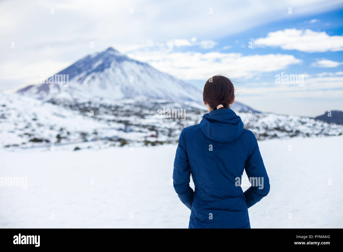 Vista posteriore del viaggiatore donna godere di neve montagne con vulcano El Teide sullo sfondo. Inverno in Isole Canarie Foto Stock