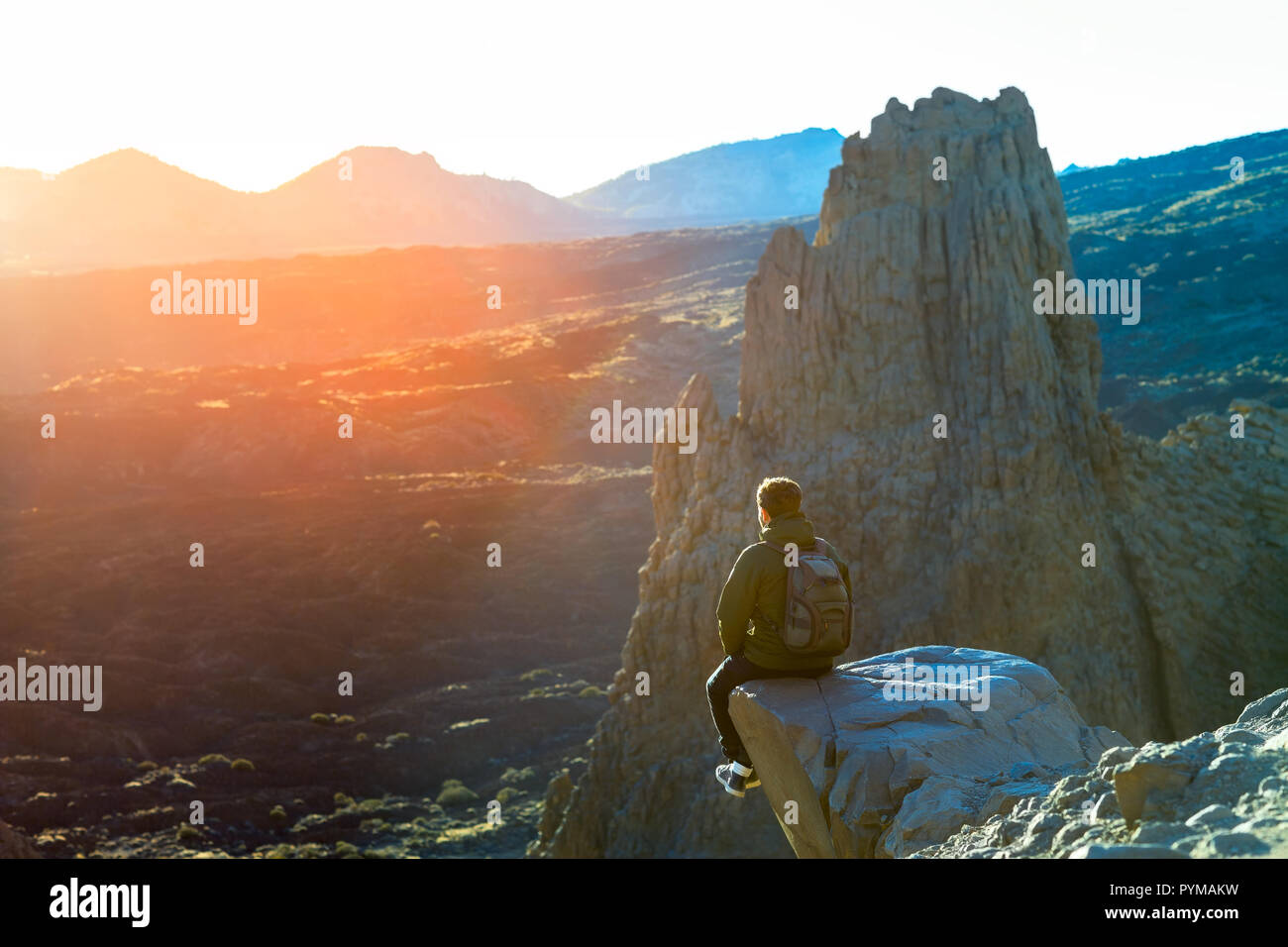 Viaggiatore giovane uomo seduto sul ciglio della scogliera e godetevi il tramonto in montagna. Concetto di viaggio Foto Stock