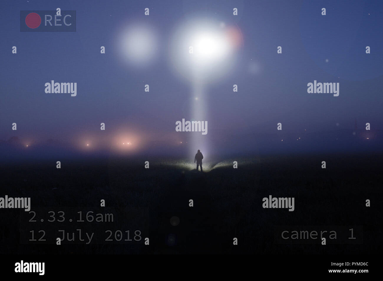 Una foto di notte come un UFO brilla verso il basso su una silhouette di una solitaria figura in piedi in un campo di nebbia. Con l'immagine catturata su TVCC Foto Stock