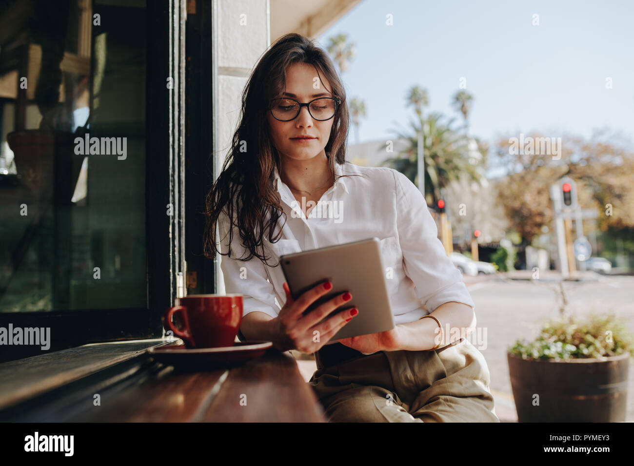 Donna seduta in un bar che lavora su un tablet digitale. donna d'affari seduta al bancone del caffè con un caffè usando un computer tablet. Foto Stock