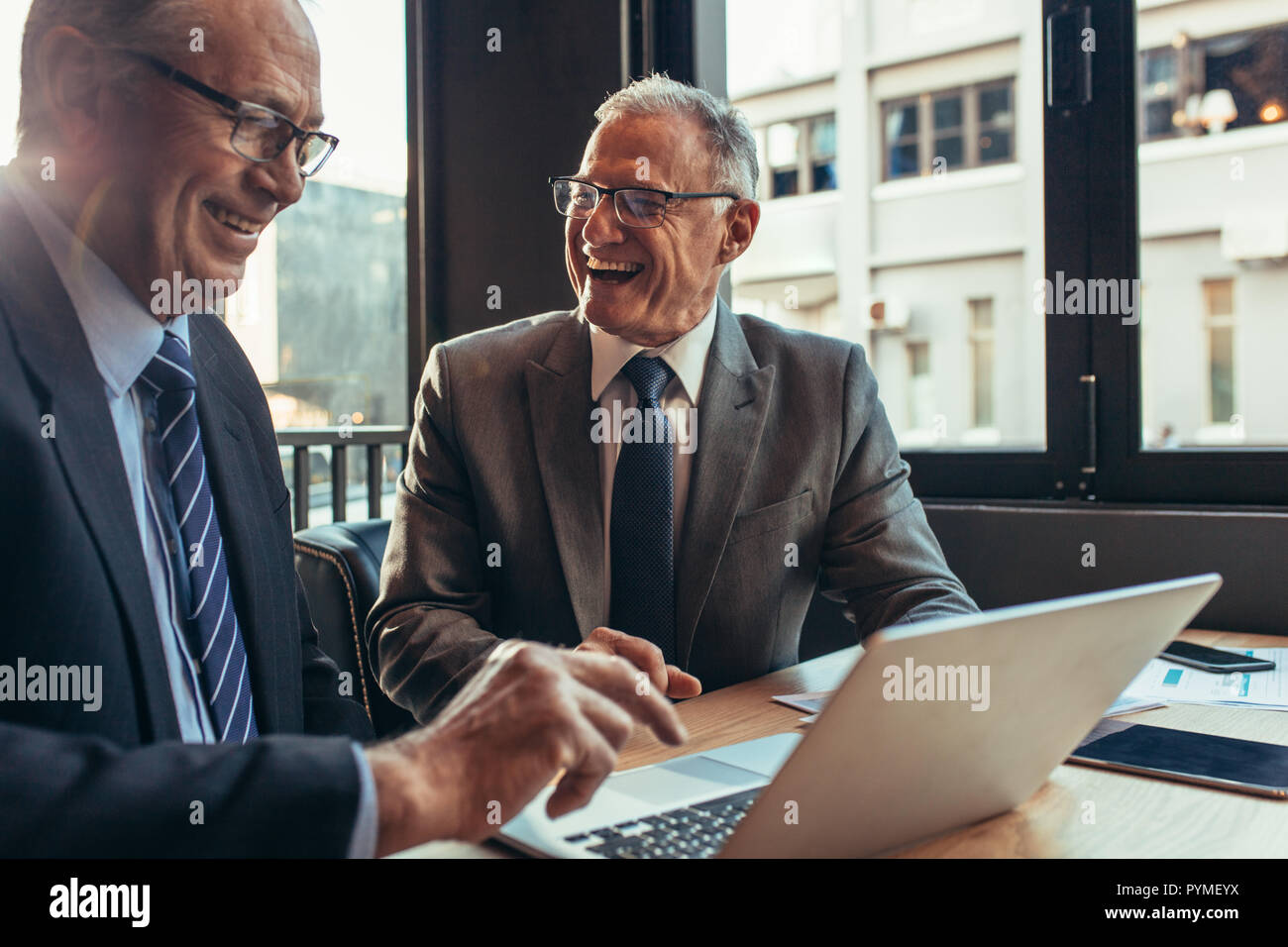 Due partner caucasici di affari presso la caffetteria. Gli imprenditori Senior udienza presso la caffetteria tabella con laptop e ridere. Foto Stock