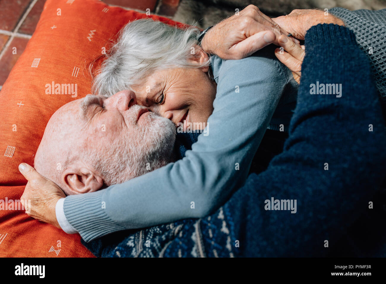 Donna sorridente dormire nelle braccia di suo marito tenendo la sua testa. Felice coppia senior di dormire sul pavimento che abbraccia ogni altra in una fredda notte. Foto Stock