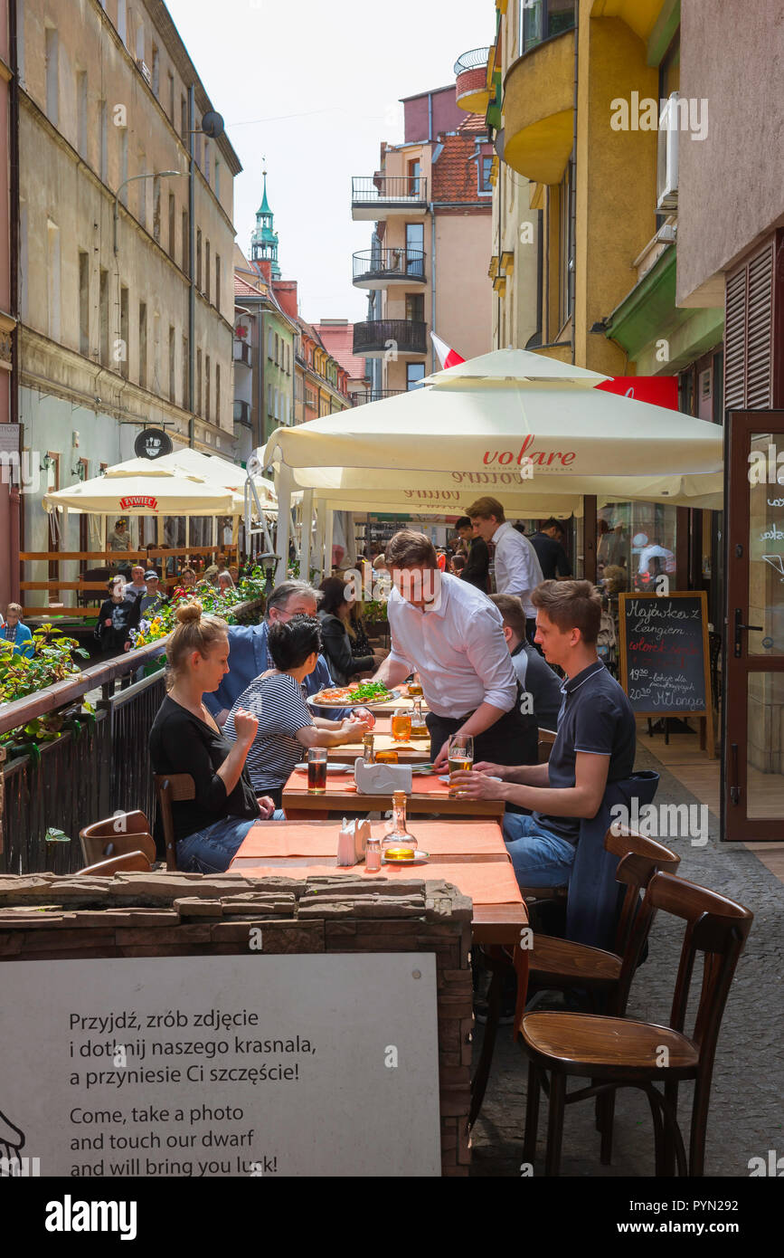 Wroclaw, vista in estate di un giovane turista giovane essendo servito il pranzo al fresco in un ristorante con terrazzo in una strada stretta a Wroclaw Old Town, Polonia. Foto Stock