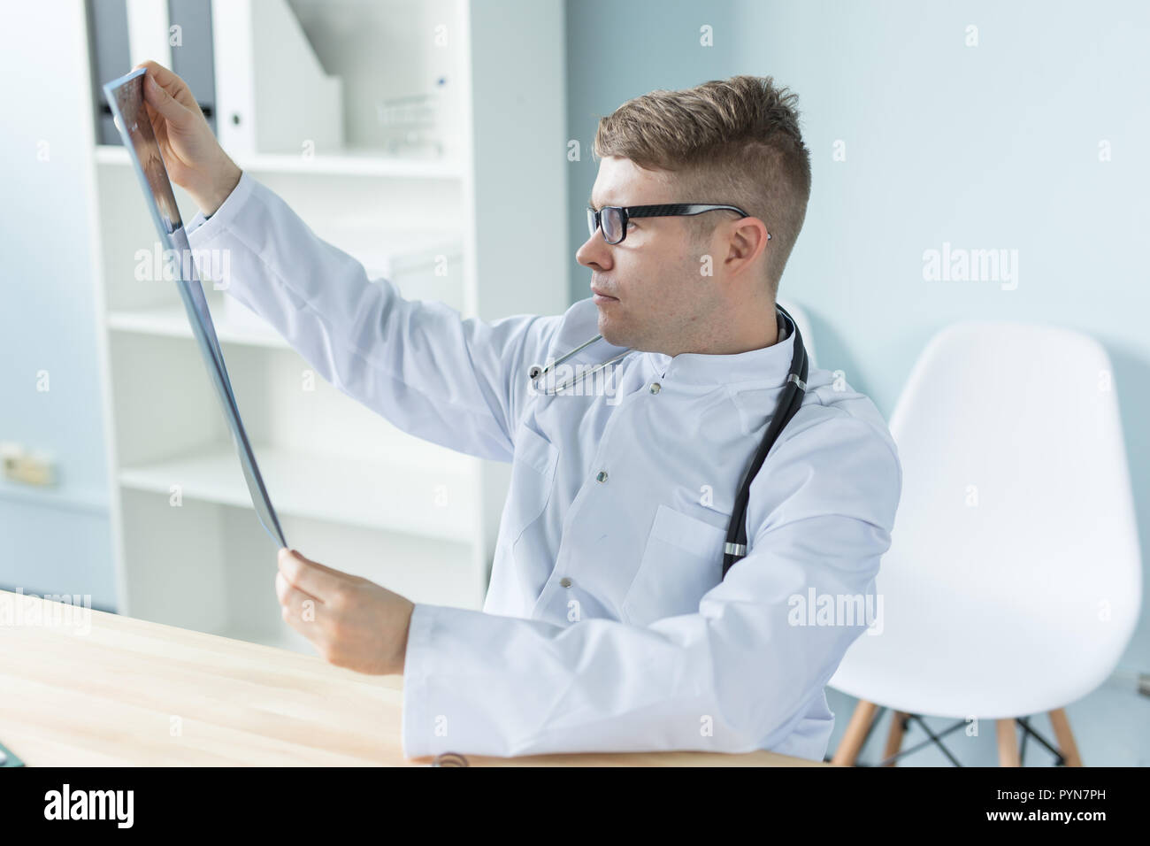 Giovane medico caucasica seduta nel suo ufficio e alla ricerca di immagini a raggi X Foto Stock