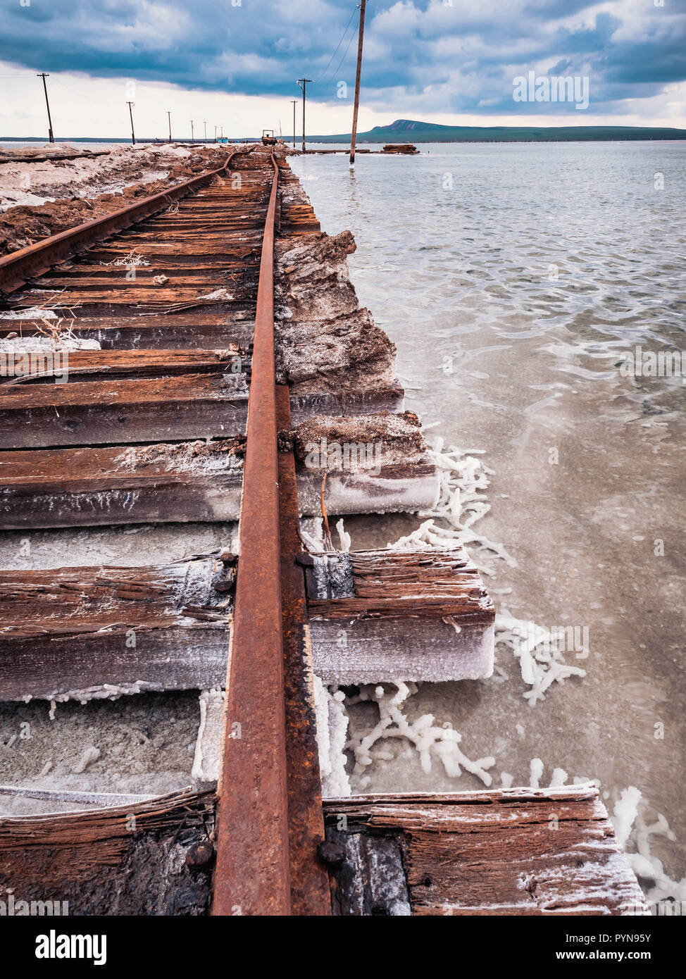 Rusty razy rotaie e traversine marcio coperto di sale sulla vecchia ferrovia tracce su una collinetta a miniere di sale vicino lago di salamoia. Foto Stock