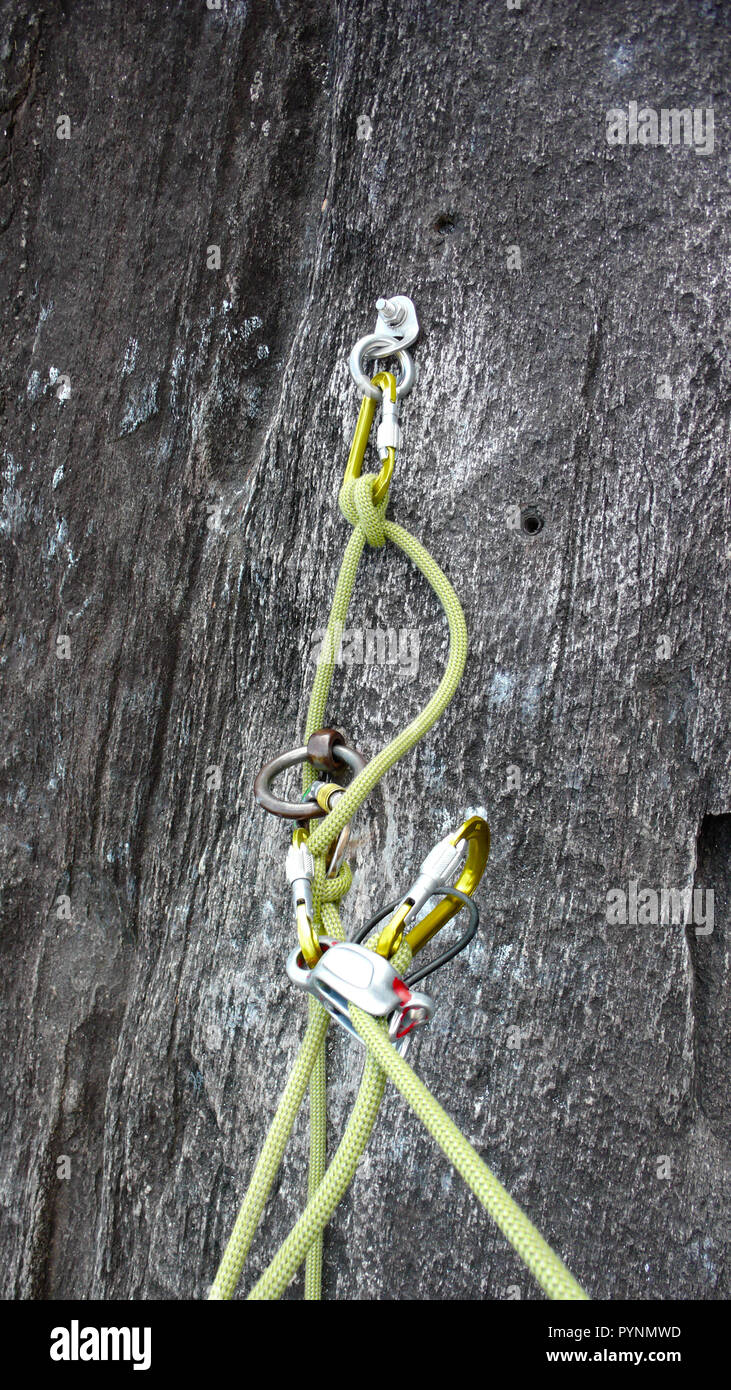Atteggiamento di assicurazione per arrampicata su roccia in granito nero con bulloni moschettoni e una corda di colore giallo Foto Stock