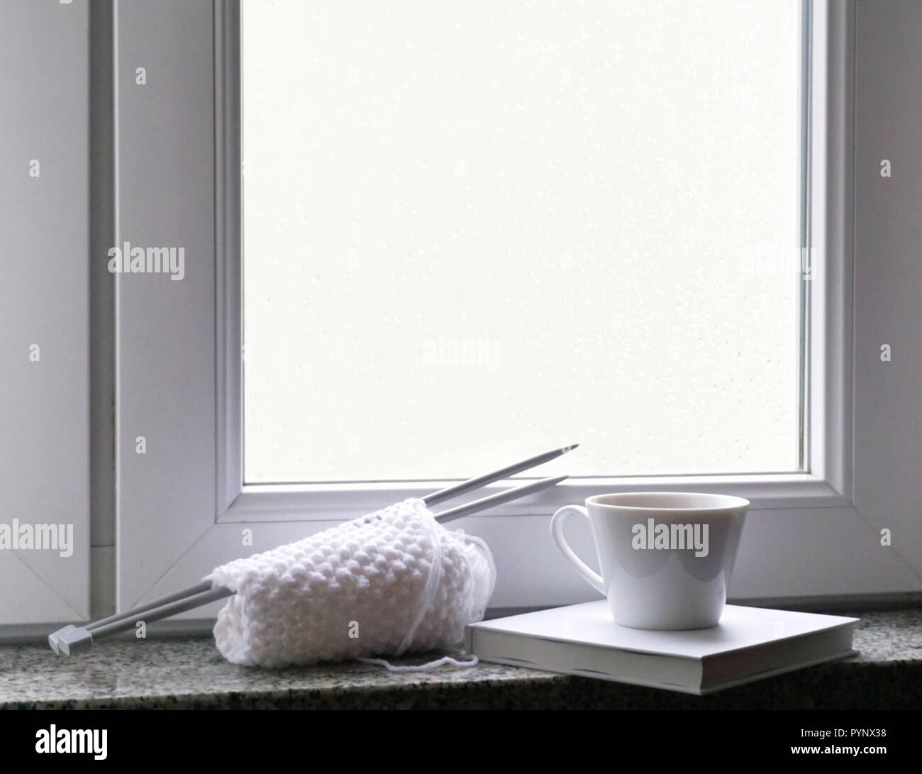 Finestra bianca telaio con gocce di pioggia su di esso e prenota, mug e tessitura sul davanzale Foto Stock