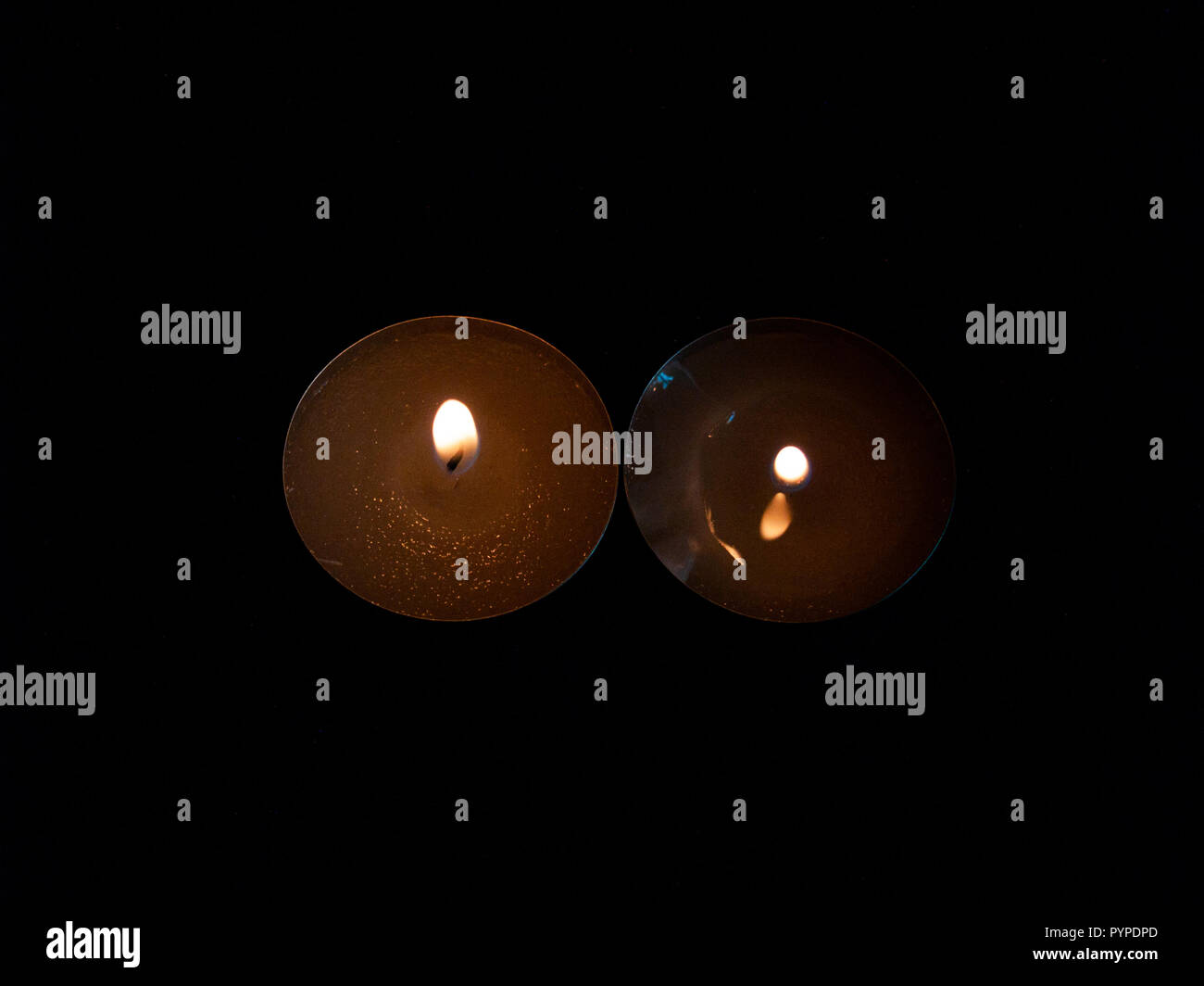 Due candele accese con una fiamma di colore arancione e isolate su uno sfondo nero Foto Stock