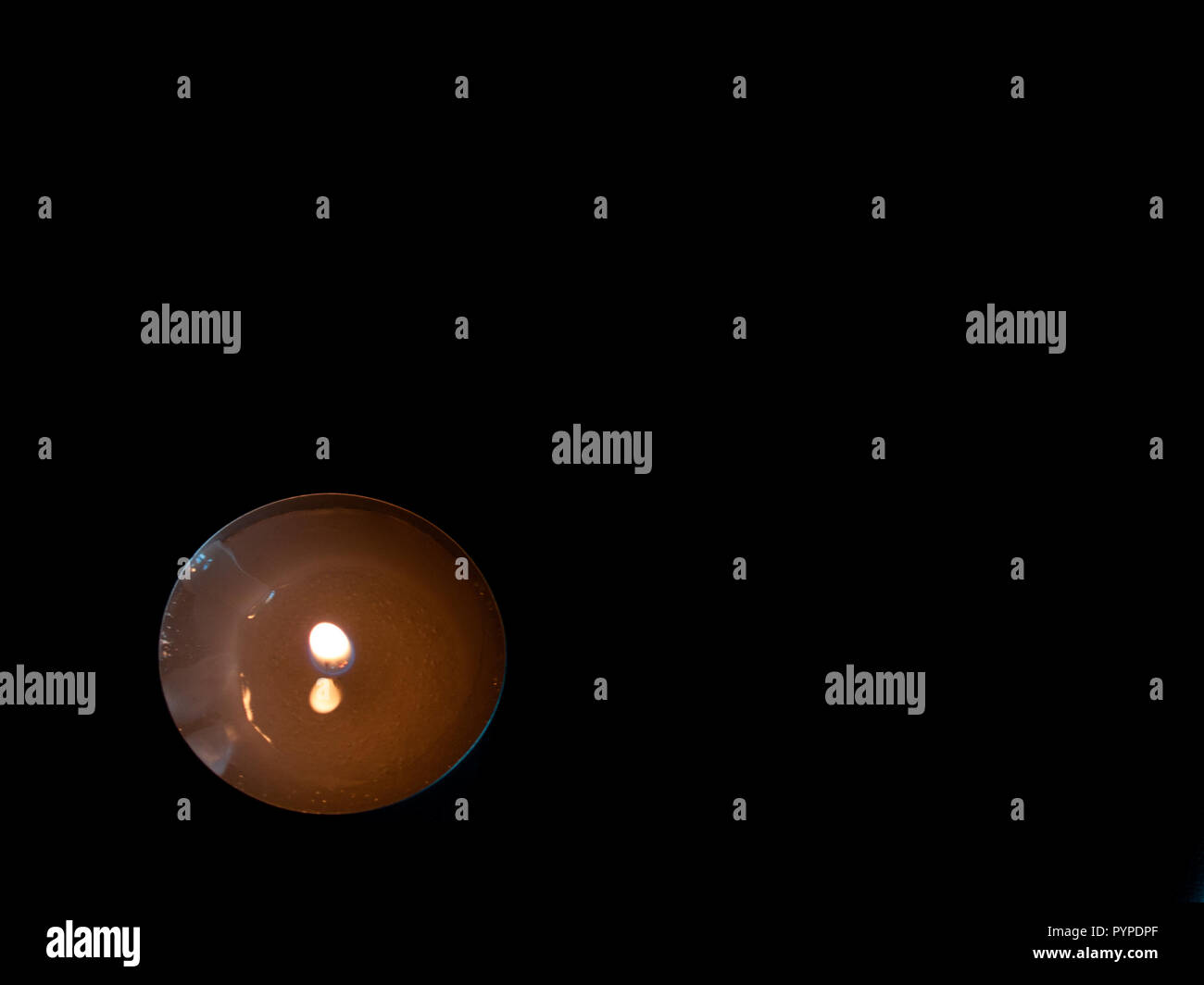 Una candela accesa con una fiamma di colore arancione e isolate su uno sfondo nero Foto Stock