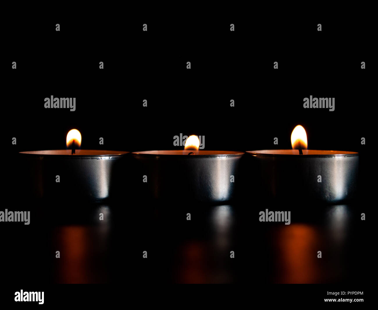 Tre candele accese con una fiamma di colore arancione e isolate su uno sfondo nero Foto Stock