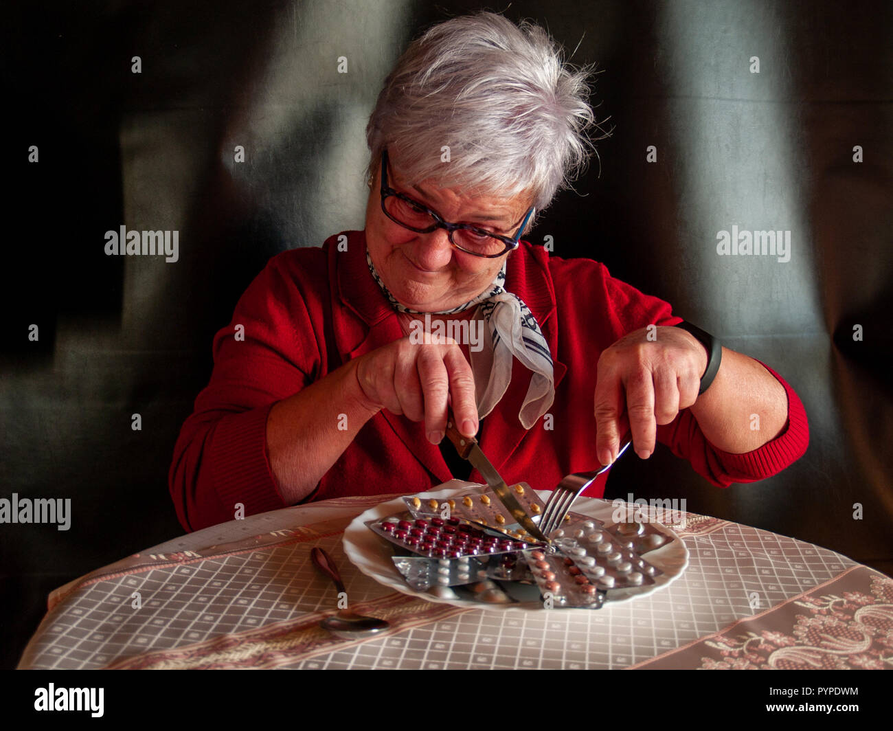 Concetto di medicina e sanità. Una donna senior il taglio di più compresse di pillole per mangiare sulla sua piastra Foto Stock