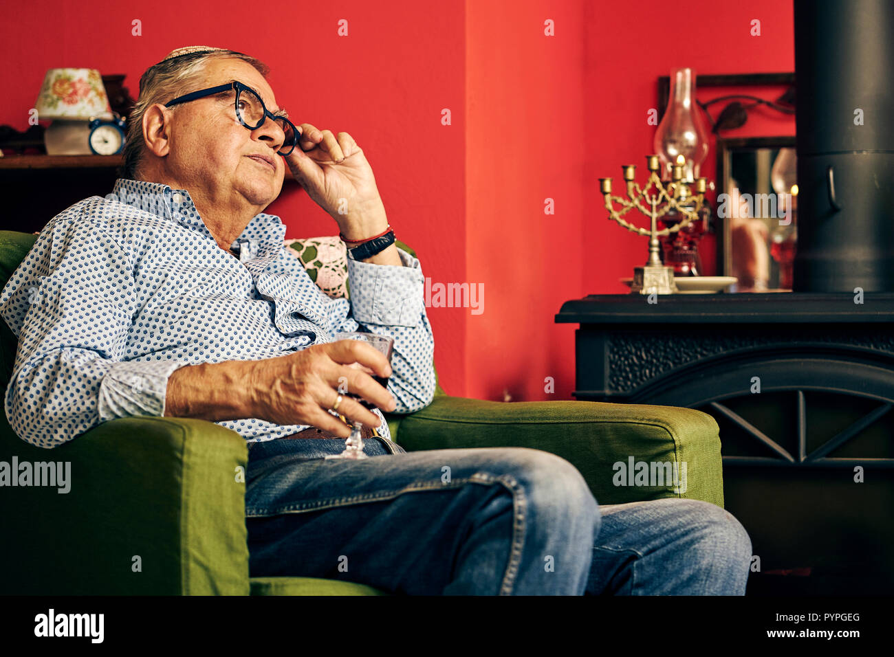 Malinconici senior ebraica seduto in poltrona e bere vino kosher Foto Stock