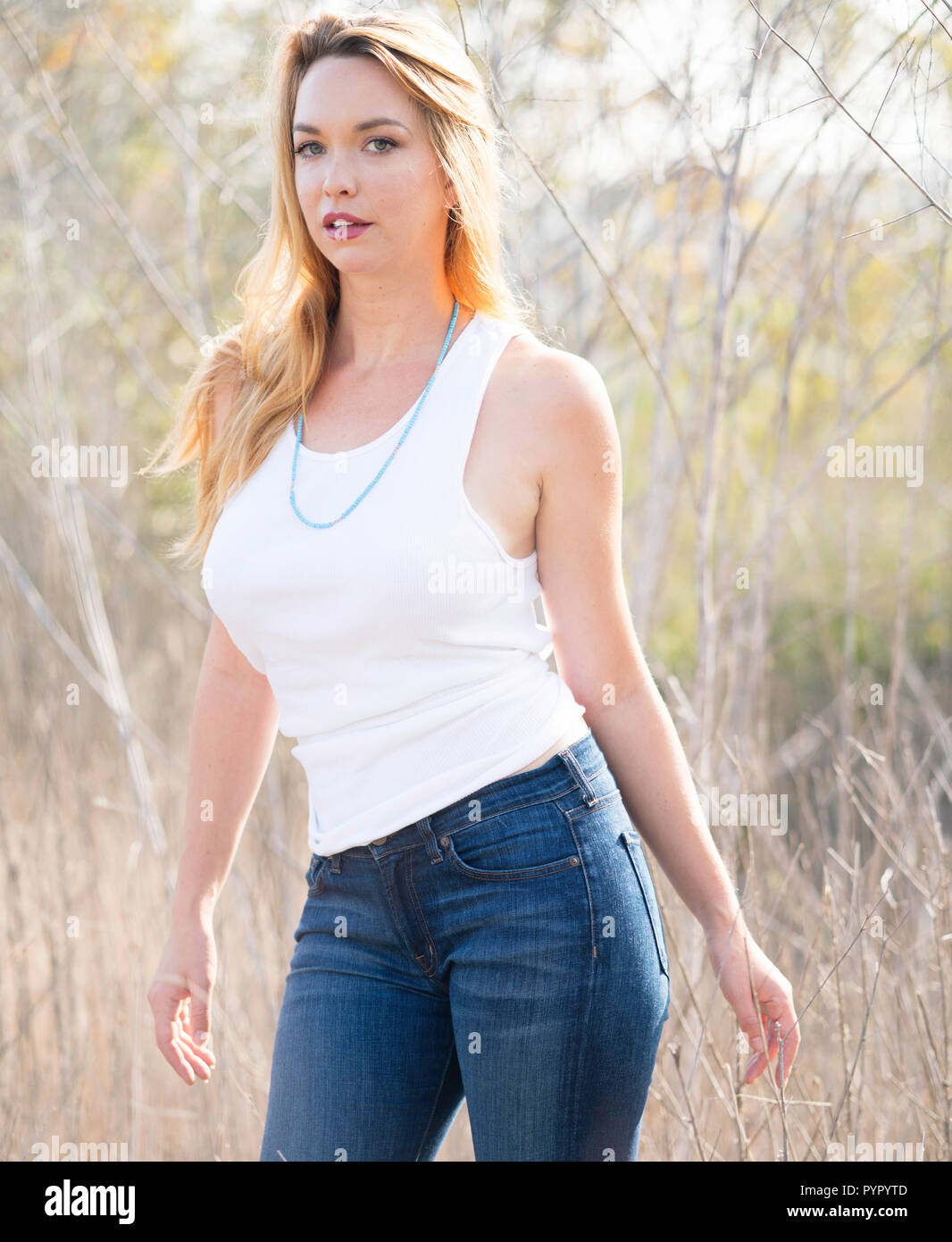 Una giovane donna pone in campo aperto che indossa una camicia bianca e  jeans blu Foto stock - Alamy