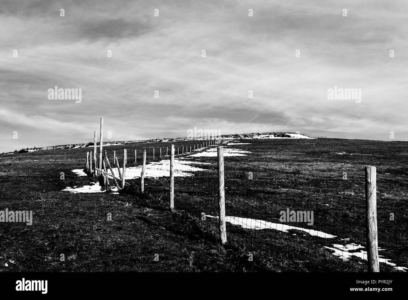 Staccionata in legno posti e filo spinato segna la linea di proprietà di una prateria con erba secca e macchie di neve sotto moody sky Foto Stock