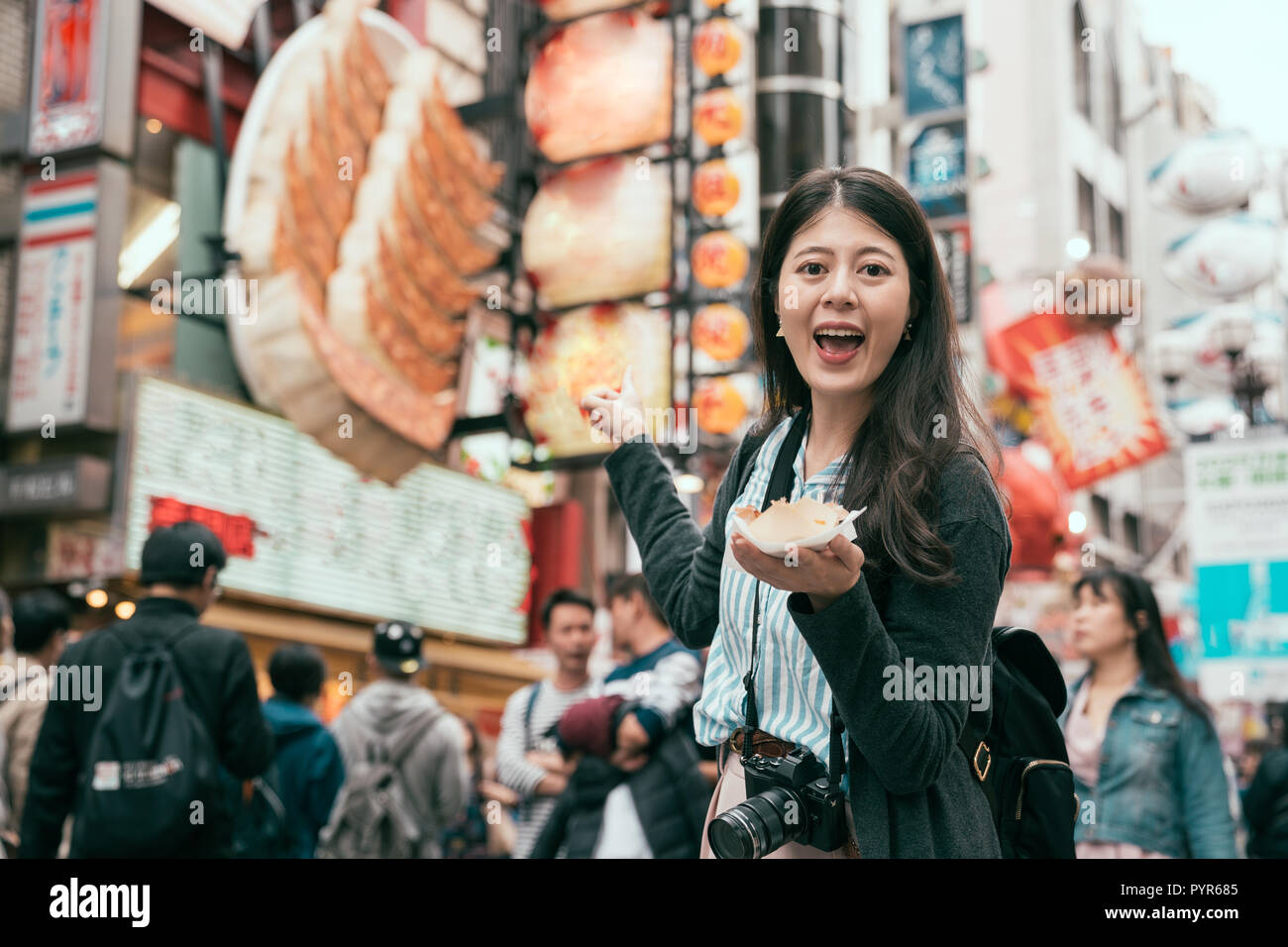 Signora giovane viaggiatore holding giapponese il cibo di strada. bella turista in piedi nella parte anteriore del negozio di gnocco in dotonbori. godere di Osaka lo stile di vita di viaggio Foto Stock