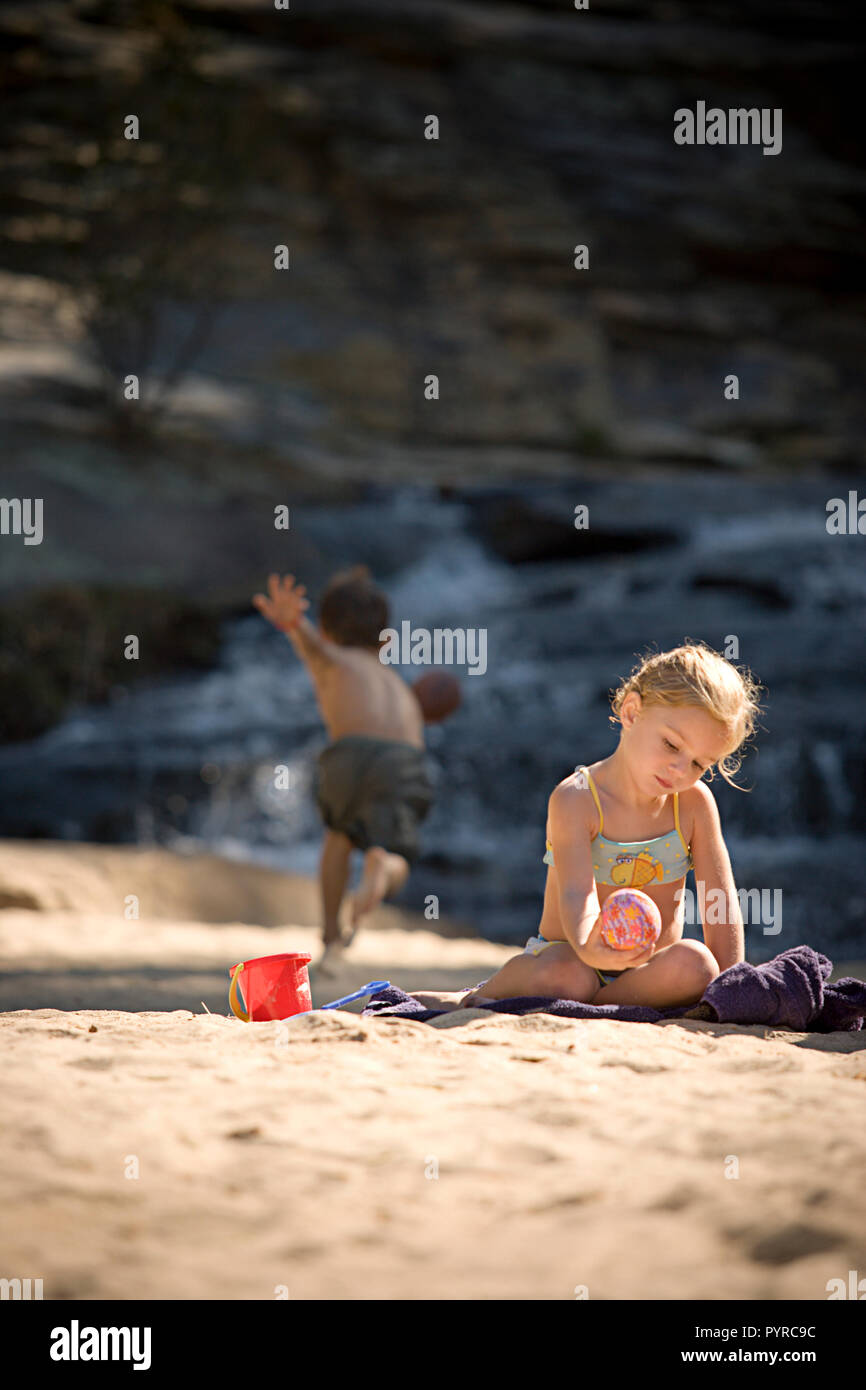Bambina giocando nella sabbia con ragazzo in esecuzione per la sfera in background Foto Stock