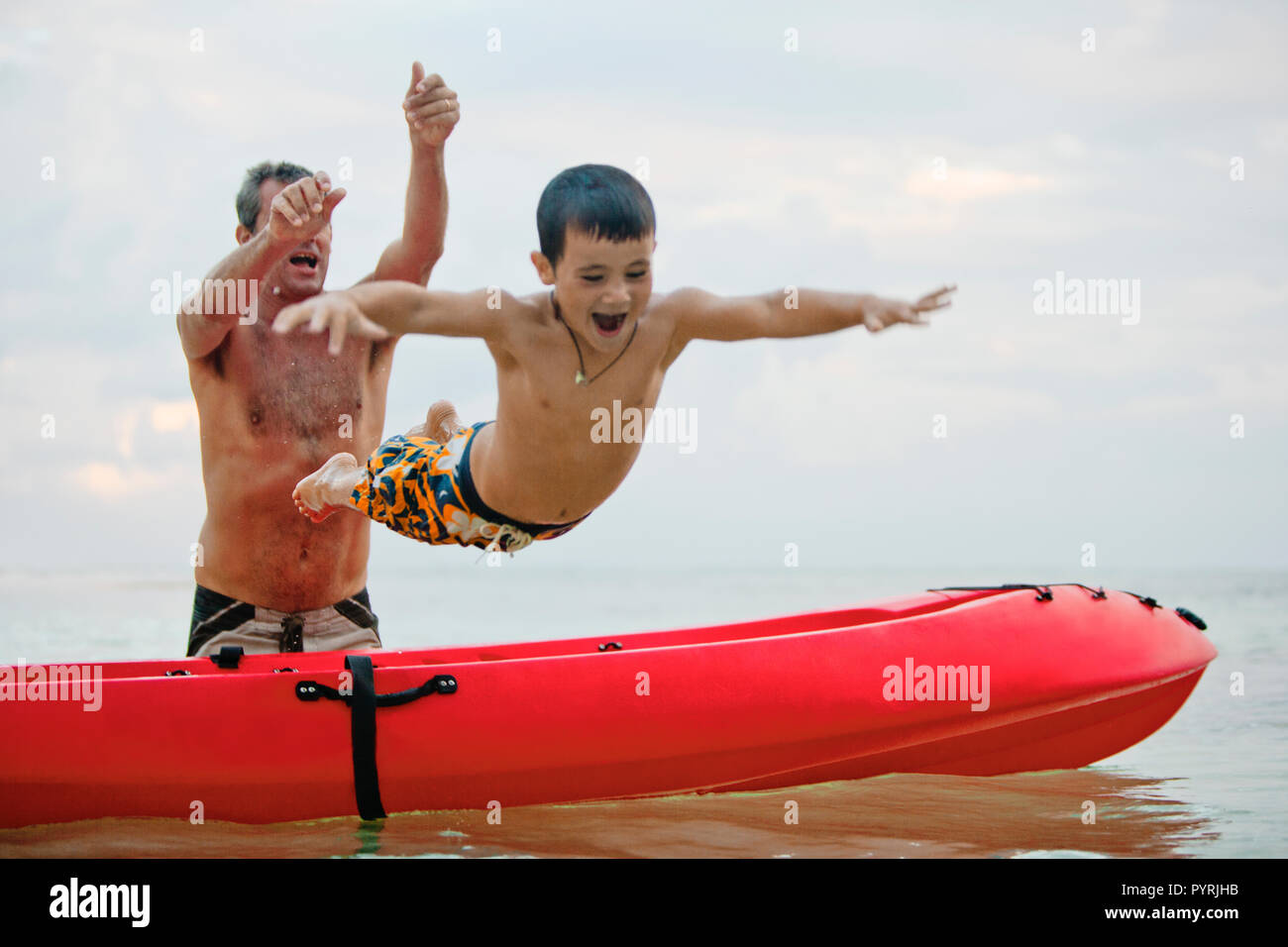 Eccitato ragazzo giovane essendo generata da un kayak da suo padre nell'oceano. Foto Stock