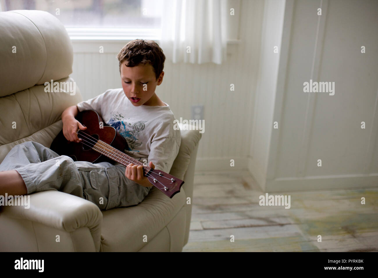 Ragazzo seduto sulla poltrona e la pratica di suonare la chitarra Foto Stock