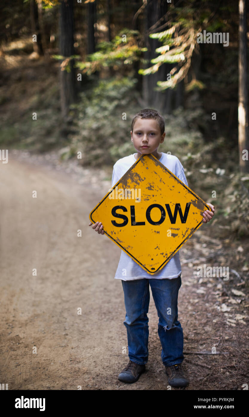 Ragazzo tenendo premuto segno lento sulla strada sterrata Foto Stock
