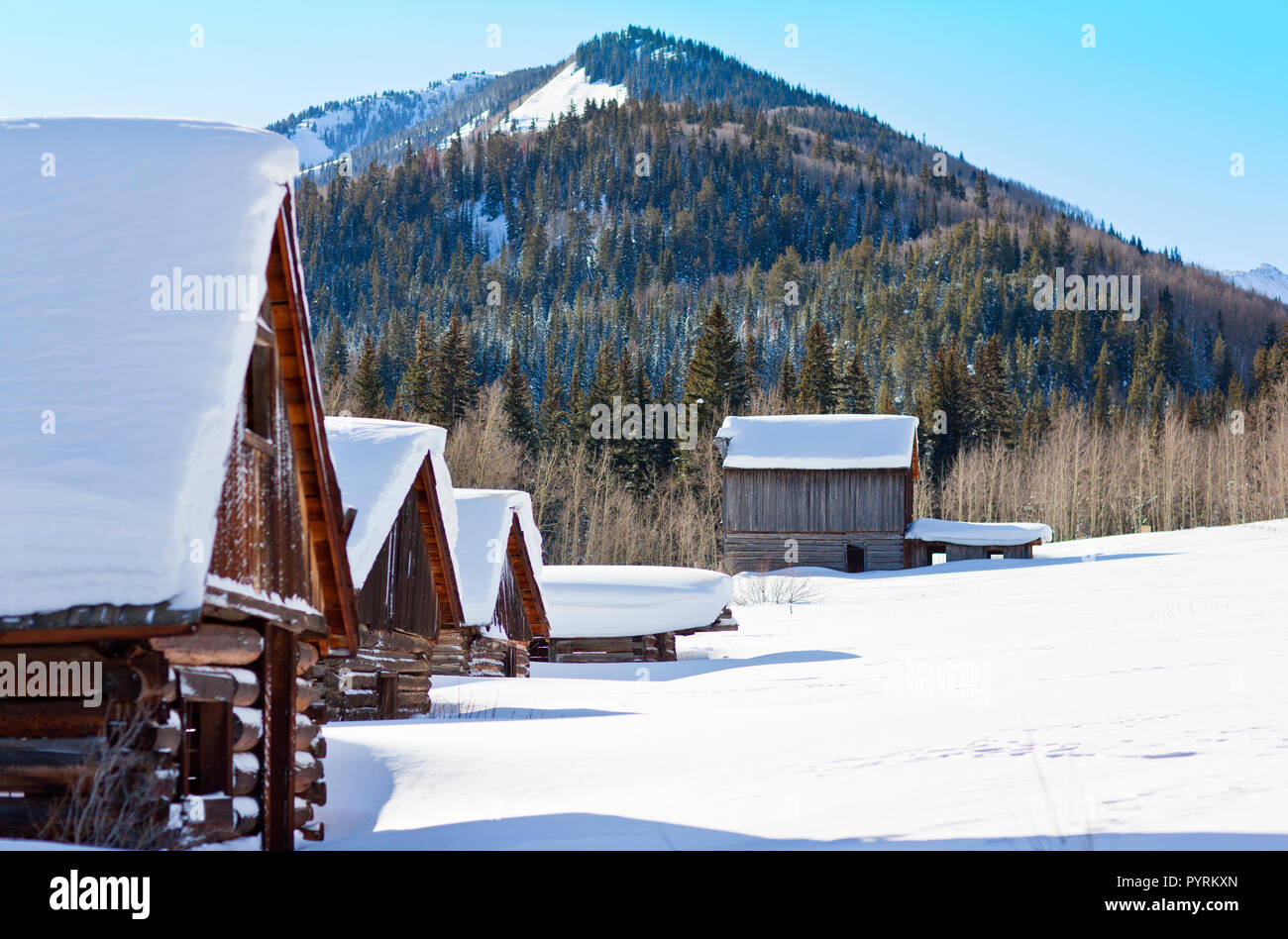 Fila di coperte di neve cabine log in una impostazione invernale. Foto Stock