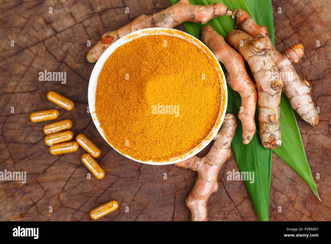 La curcuma in polvere in ciotole di legno e la curcuma capsule su sfondo di legno Foto Stock