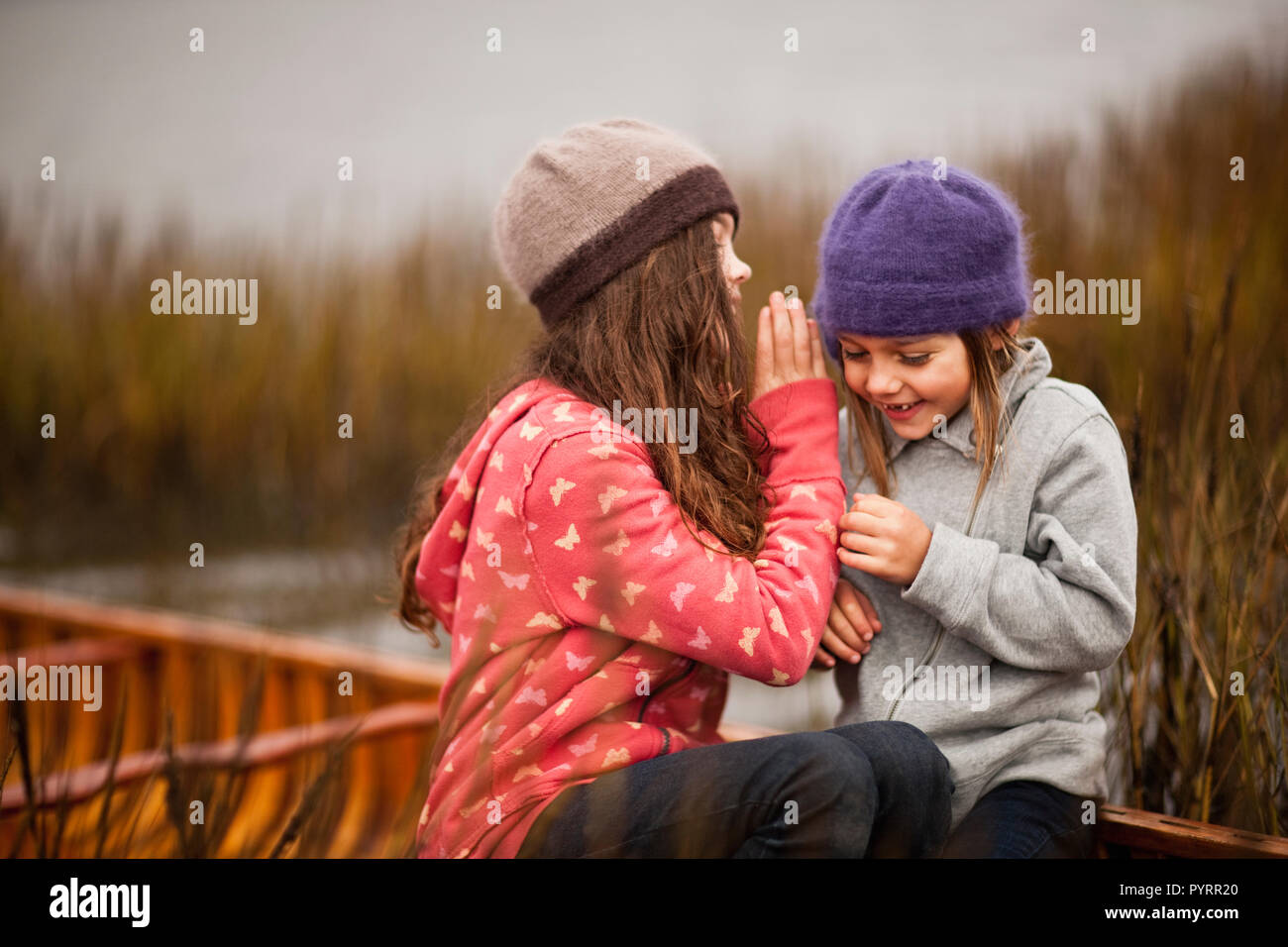 Due sorelle raccontano segreti e ridere come essi siedono insieme in una canoa di legno tra ance ance su un lago. Foto Stock