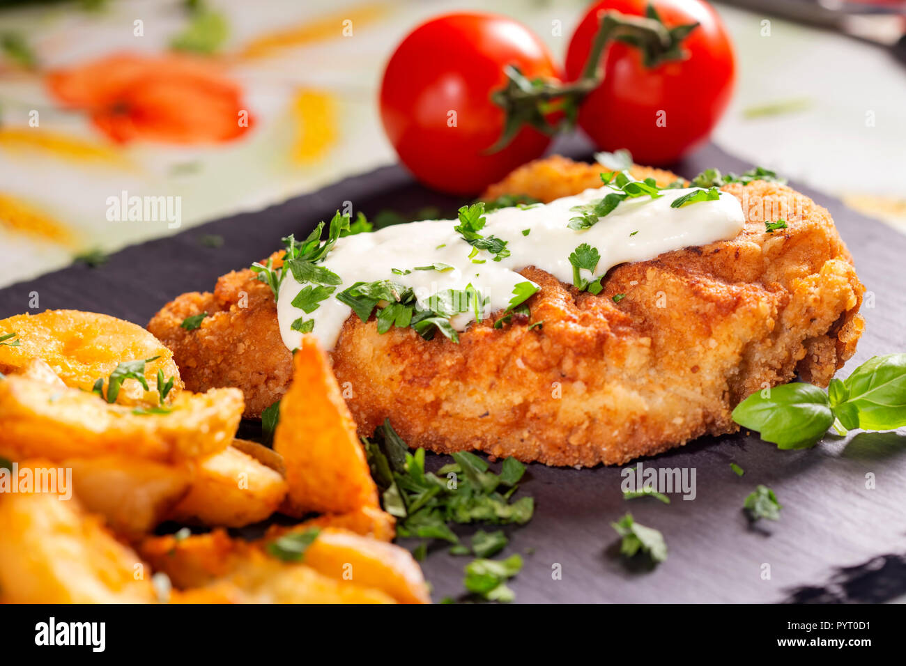 La carne di maiale schintzel con una salsa bianca, patatine fritte e erbe su una di ardesia scura Foto Stock