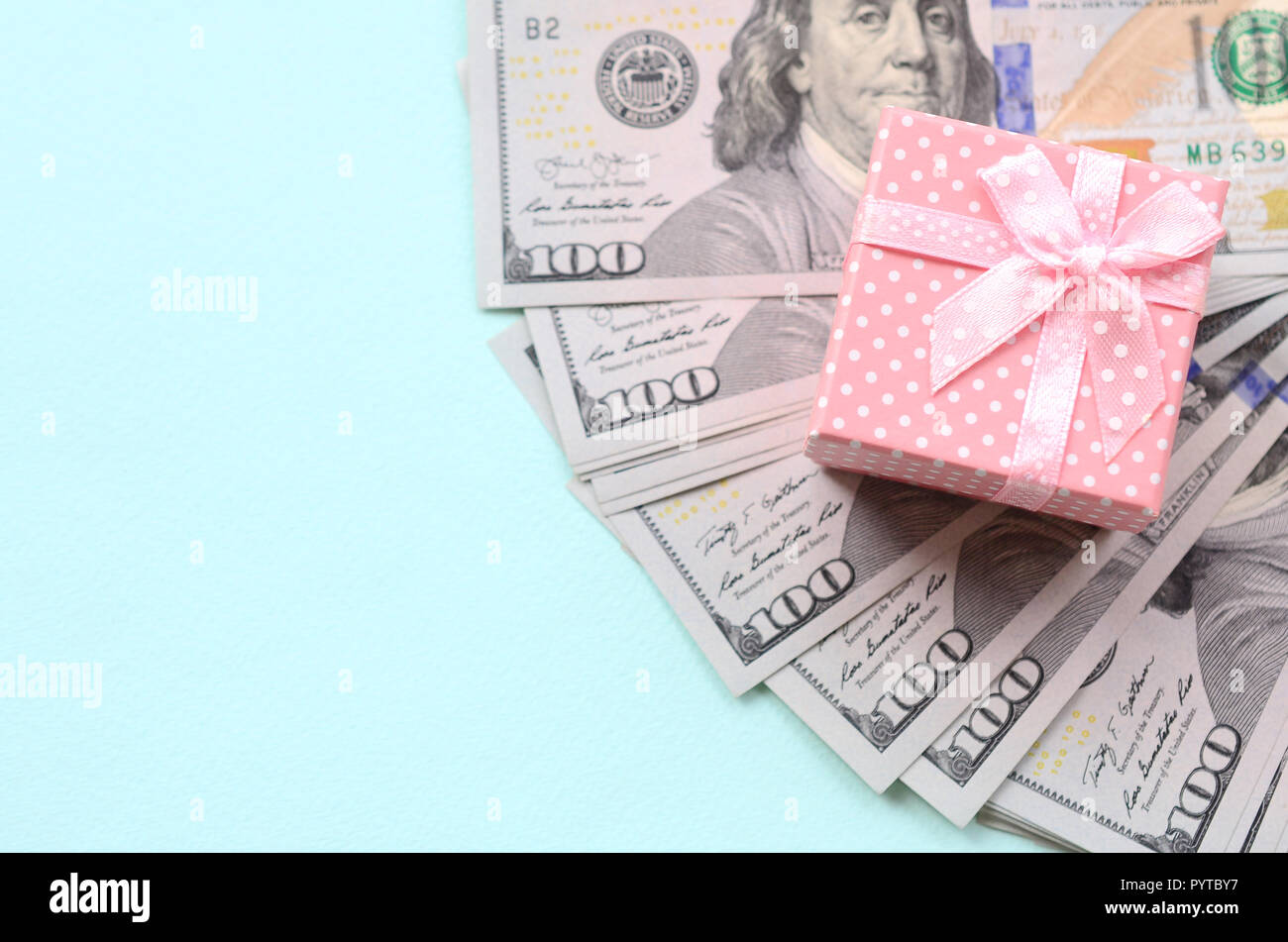 Rosa punteggiato confezione regalo si trova nei pressi di centinaia di dollari su un fondo azzurro. Foto Stock