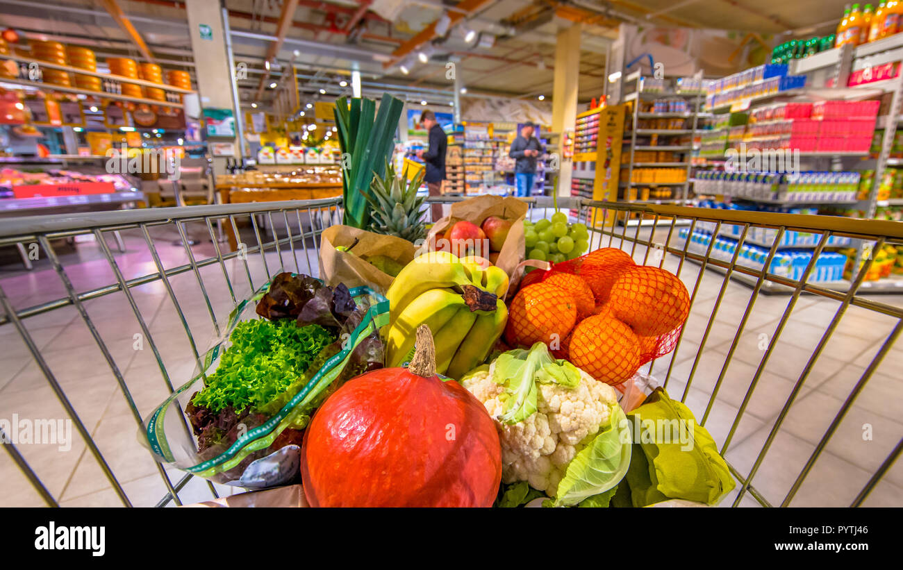 Negozio di alimentari carrello nel supermercato riempiti con prodotti freschi e salutari e di prodotti alimentari come visto dai clienti il punto di vista con la gente di shopping in backg Foto Stock